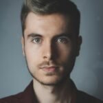 Close-up portrait of a young man with facial hair and a serious expression.